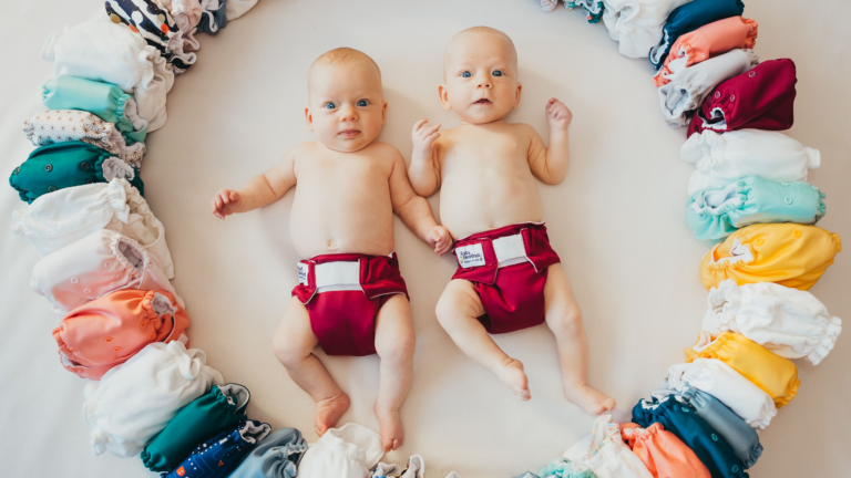 Two babies wearing reusable nappies lying in a circle of reusable nappies