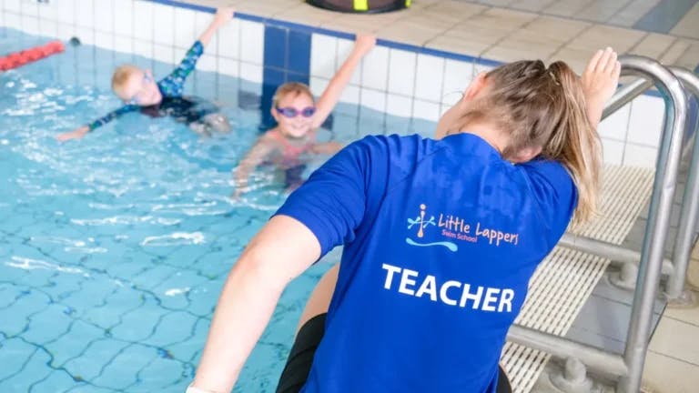Instructor demonstrating a swim stroke to two children in the pool