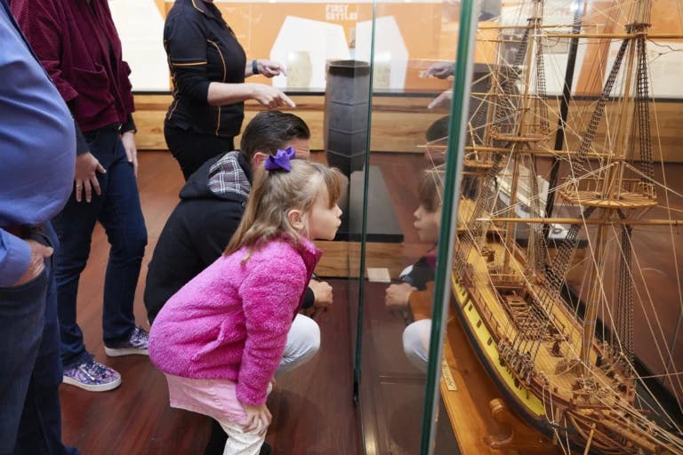Little girl in pink shirt stares at wooden ship