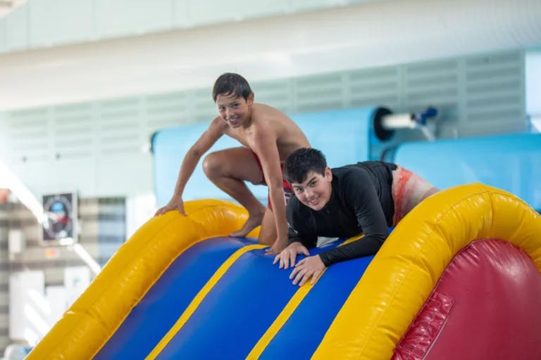 Two boys on top of an inflatable in the pool