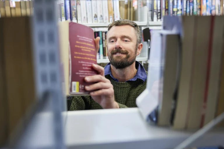 man viewed through bookshelf picking up book from shelf