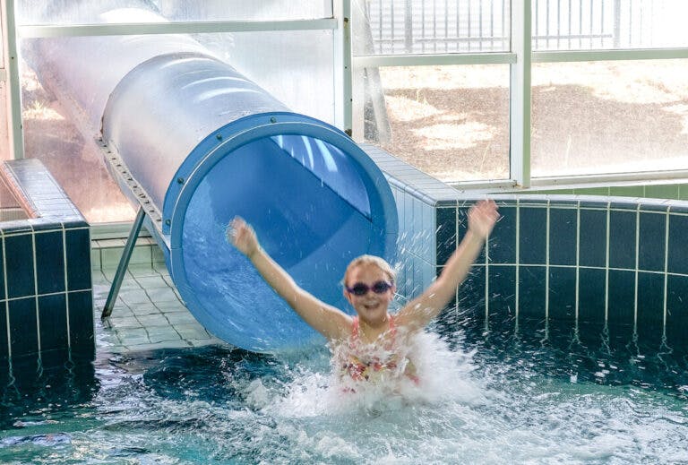 Young boy exiting waterslide tube into pool with a splash